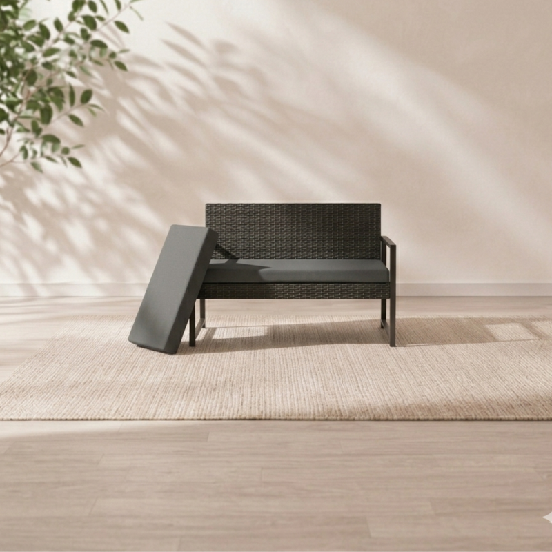 Black outdoor bench cushion displayed on a modern woven garden loveseat in a minimal sunlit home setting